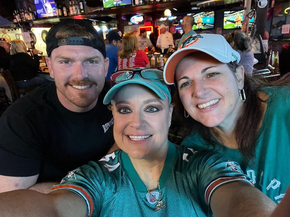 Three regulars in Dolphins jerseys smiling at the bar