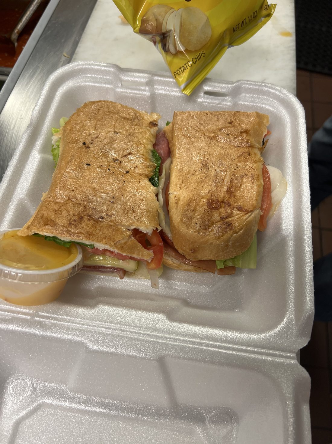 Italian sub stacked with meats lettuce and tomato, with chips