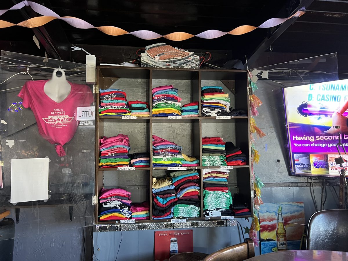 The merch wall at Kelly's stacked with folded tees sorted by size
