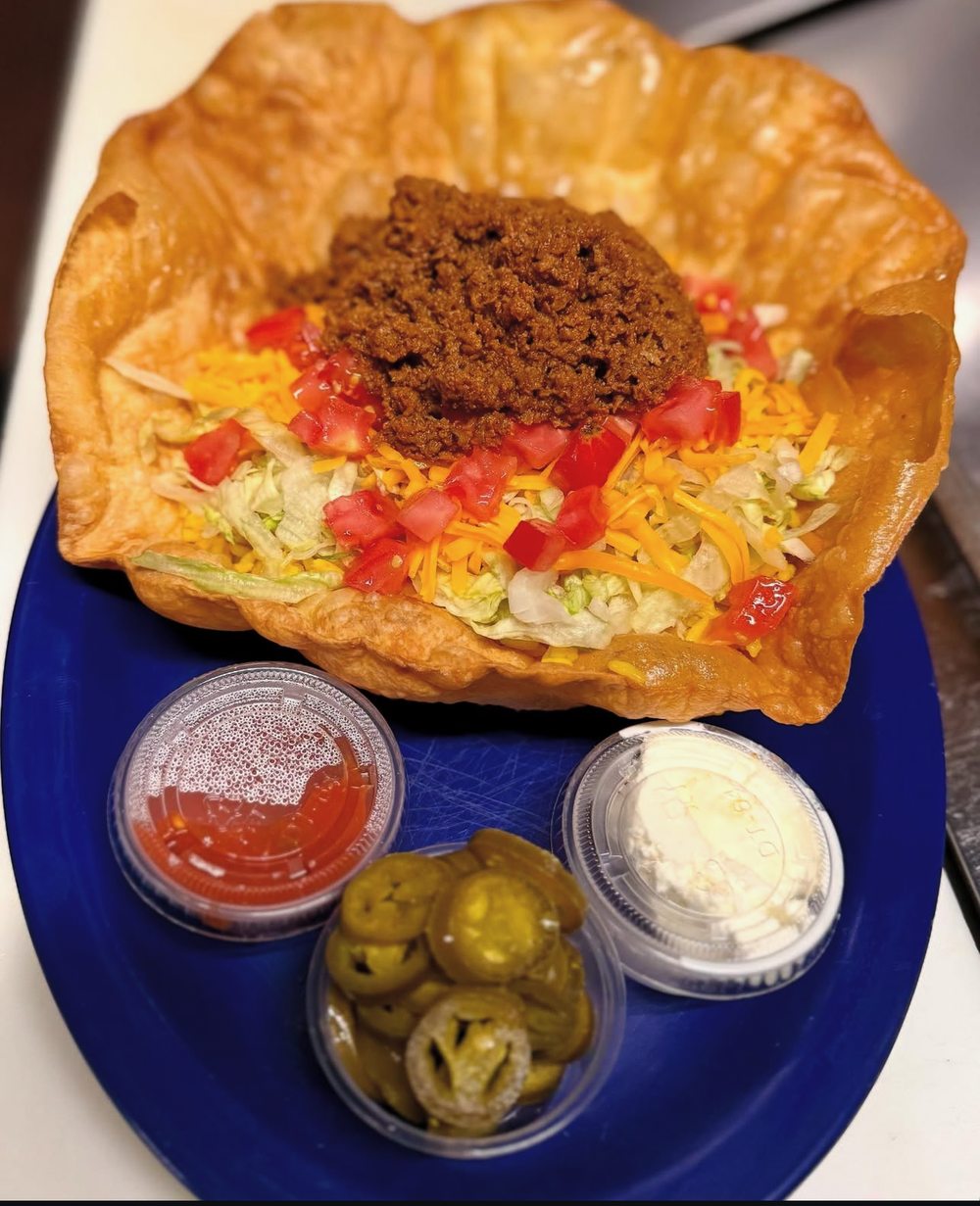 Taco salad in a fried tortilla bowl with jalapeños sour cream and salsa